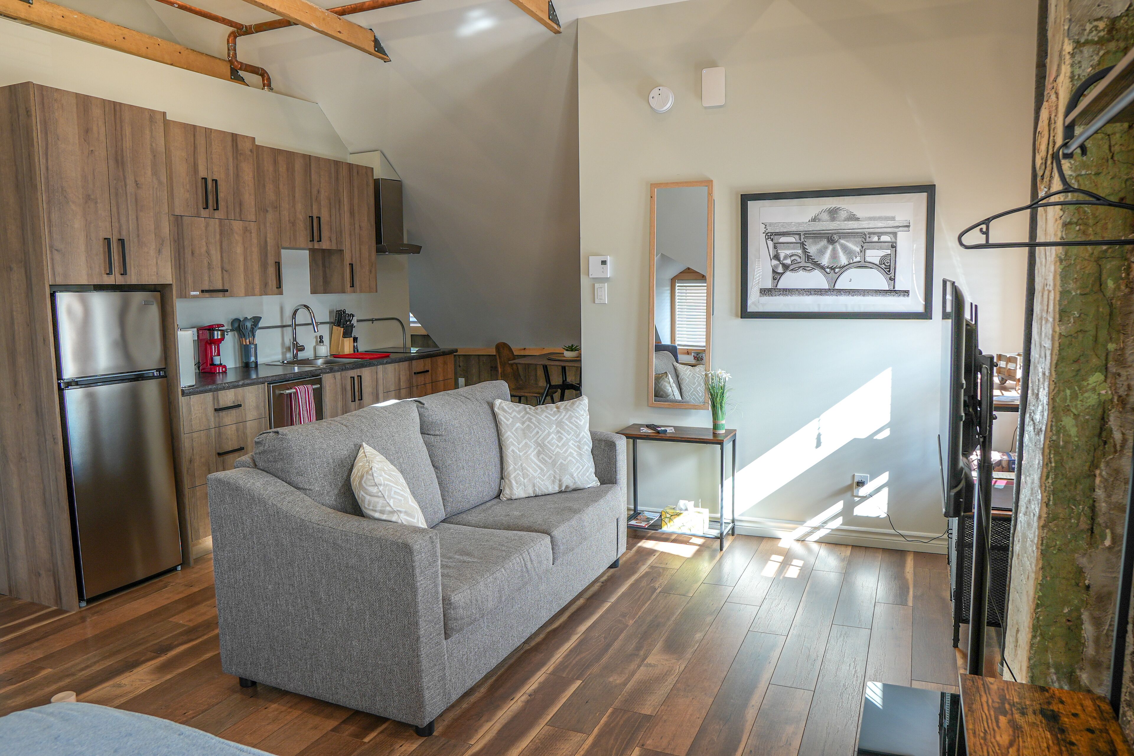 A modern kitchen with wooden cabinets, a stainless steel refrigerator, and a dining area with a gray sofa.