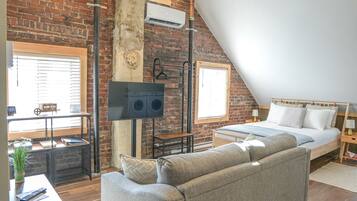 Un dormitorio estilo loft con pared de ladrillo, una cama grande, un televisor y un sofá.
