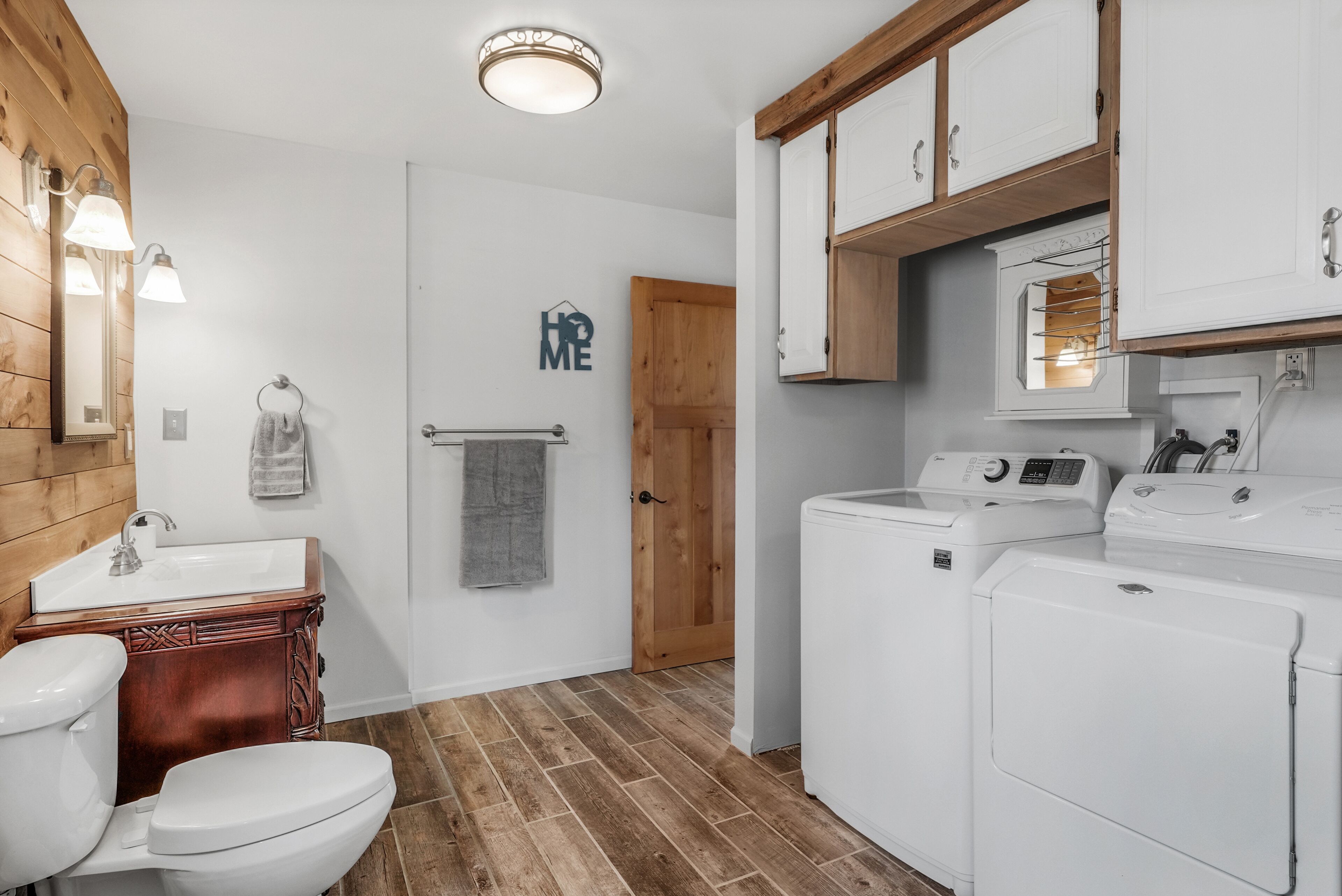 Un baño con tocador de madera, inodoro, lavamanos y lavadora.