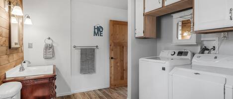 Un baño con tocador de madera, inodoro, lavamanos y lavadora.