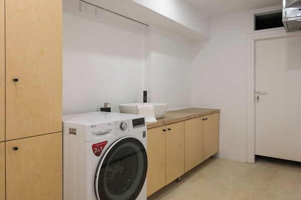 A laundry room with a front-loading washing machine, a sink, and wooden cabinets.