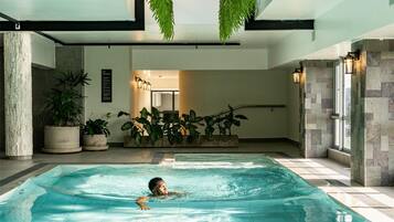 Una piscina interior con tragaluces, plantas en macetas y una persona nadando.