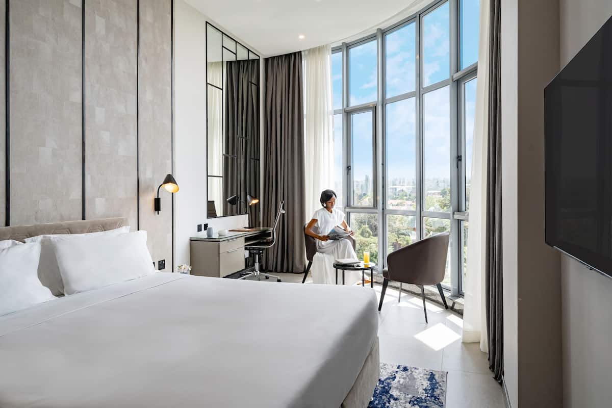 Une chambre d’hôtel moderne dotée d’un grand lit, d’un bureau, d’une chaise et d’une grande fenêtre donnant sur la ville.