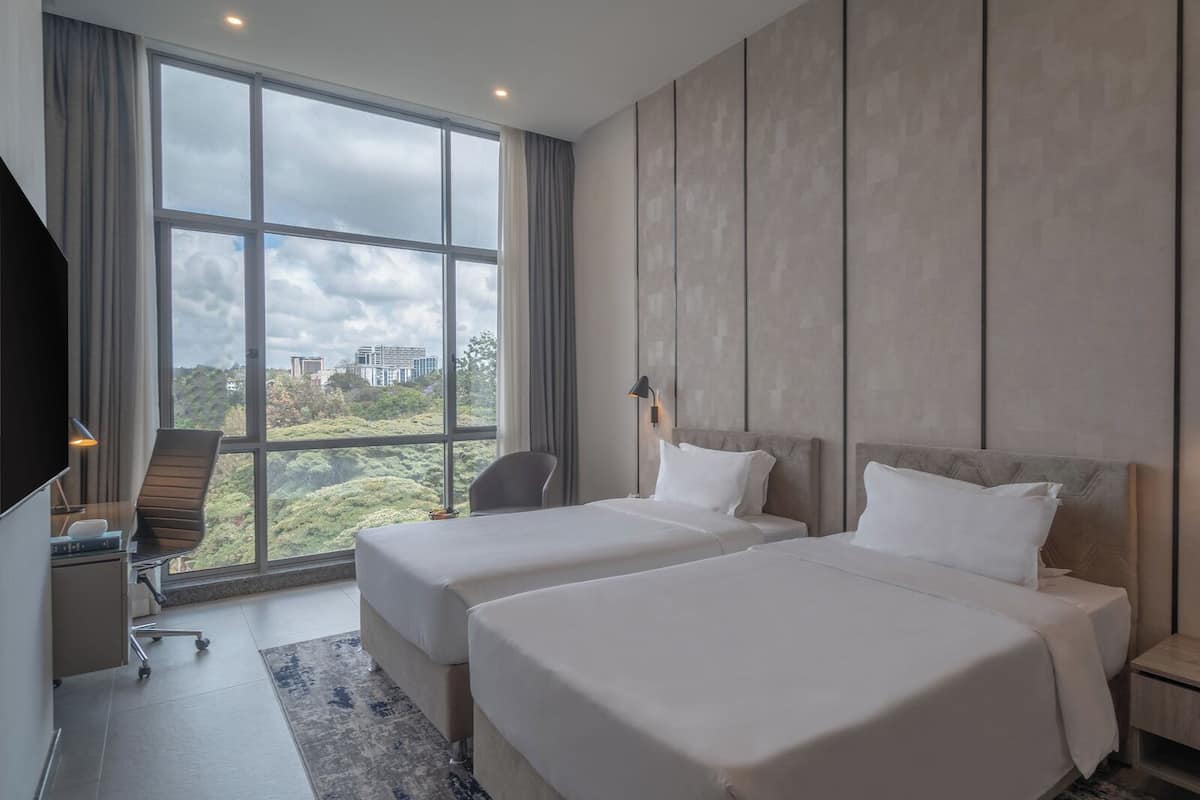 Une chambre d’hôtel moderne avec deux lits, un bureau et une grande fenêtre donnant sur la ville.