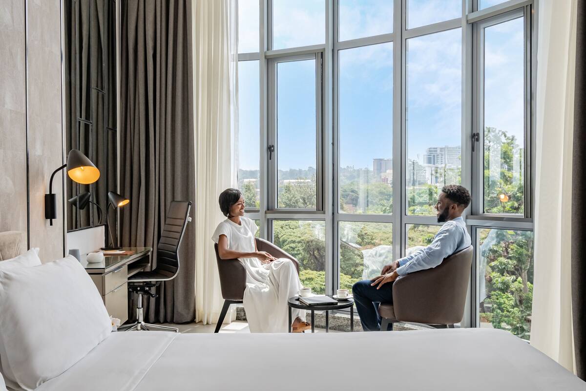 Une chambre d’hôtel moderne dotée d’un grand lit, d’un bureau avec une chaise, d’une lampe et offrant une vue sur la ville grâce à de grandes fenêtres.