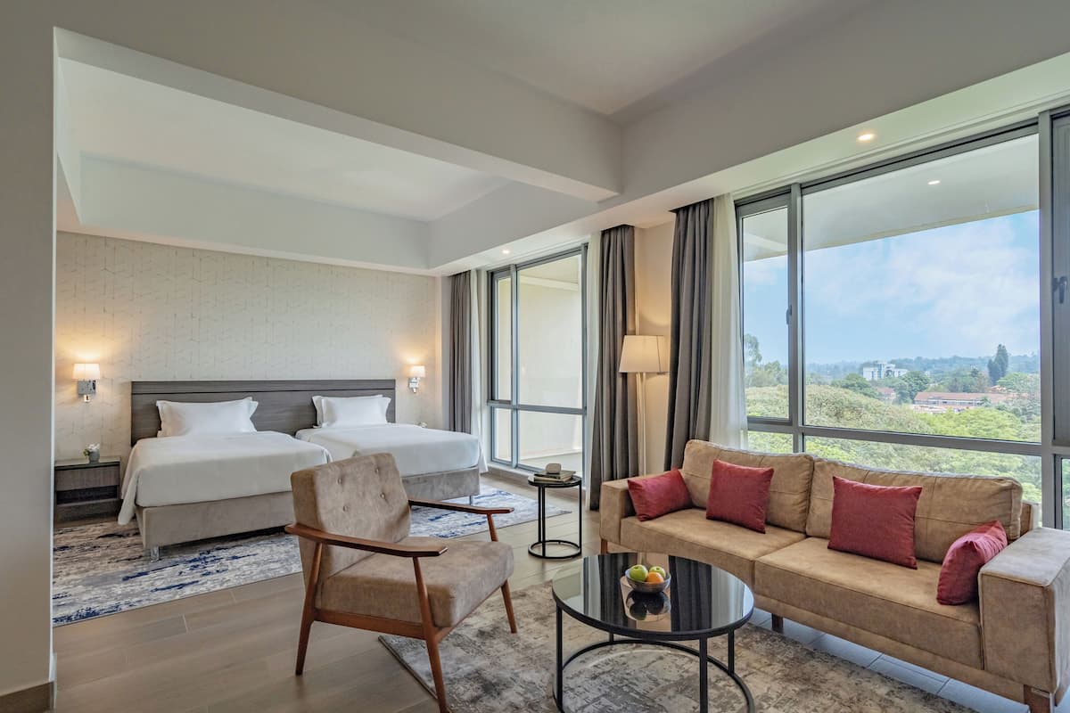 Une chambre d’hôtel avec deux lits, un canapé, une table basse et de grandes fenêtres donnant sur le paysage.