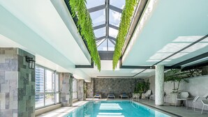 An indoor swimming pool with a glass ceiling, stone walls, and lounge chairs along the sides.