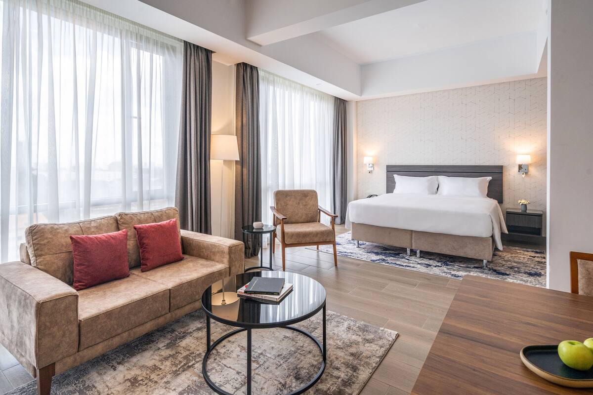 Une chambre d’hôtel avec un lit, un canapé, une chaise, une table basse et une table à manger avec des pommes.