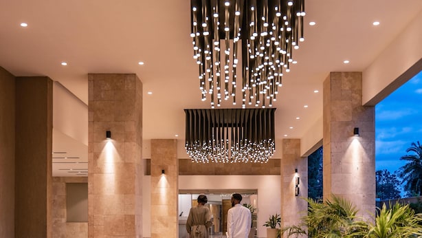 A modern hotel lobby with a central column, a hanging light fixture, and a view of the outdoors.