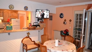 Una cocina acogedora con armarios de madera, una mesa de comedor con mantel floreado y un televisor montado en la pared.