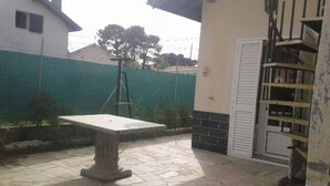 Un patio con una mesa de piedra, una puerta blanca y una valla verde al fondo.