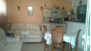 Una sala de estar con un sofá color beige, una mesa de comedor con sillas y una cocina con armarios y un refrigerador.