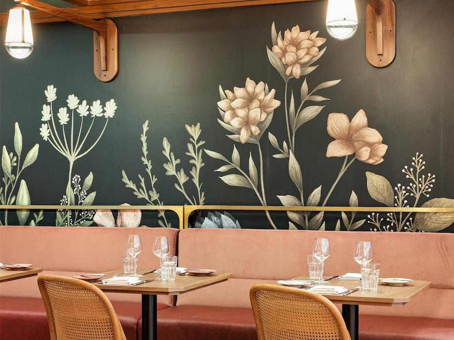 Interior de restaurante com painéis de madeira, um mural de flores e um chão estampado.