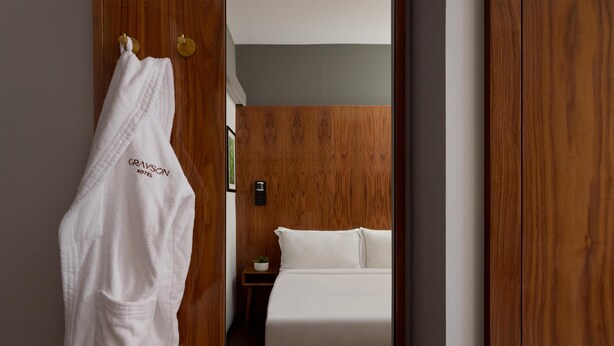 A hotel room with a wooden wardrobe, a white robe hanging on the door, and a bed with white bedding. - Grayson Hotel in the Unbound Collection by Hyatt (New York)