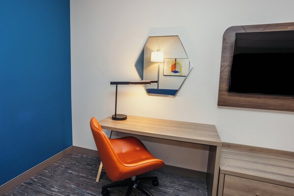 A modern office space with a desk, an orange office chair, a hexagonal mirror, and a wall-mounted lamp.
