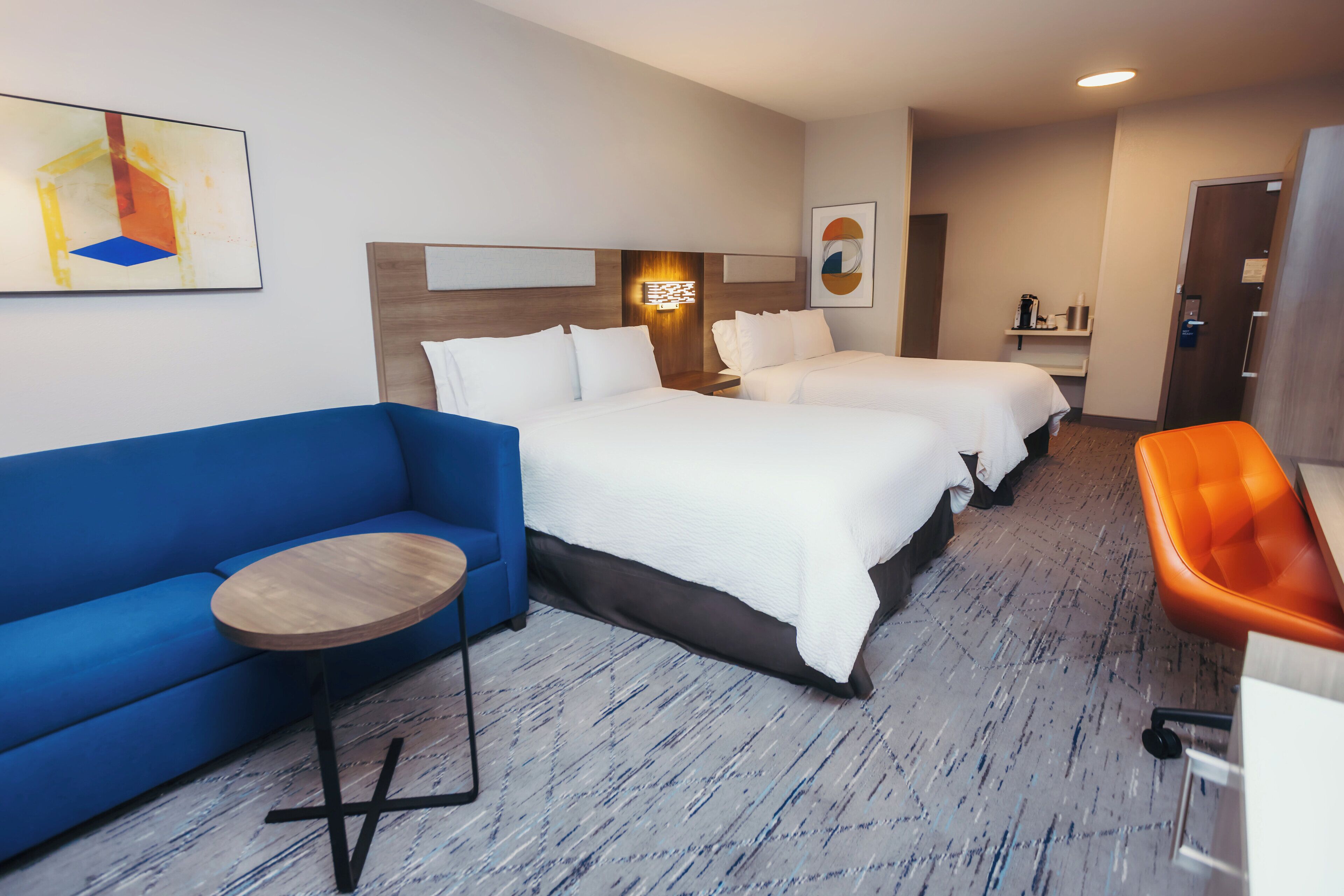 A hotel room with two beds, a blue sofa, a small round table, and an orange chair.