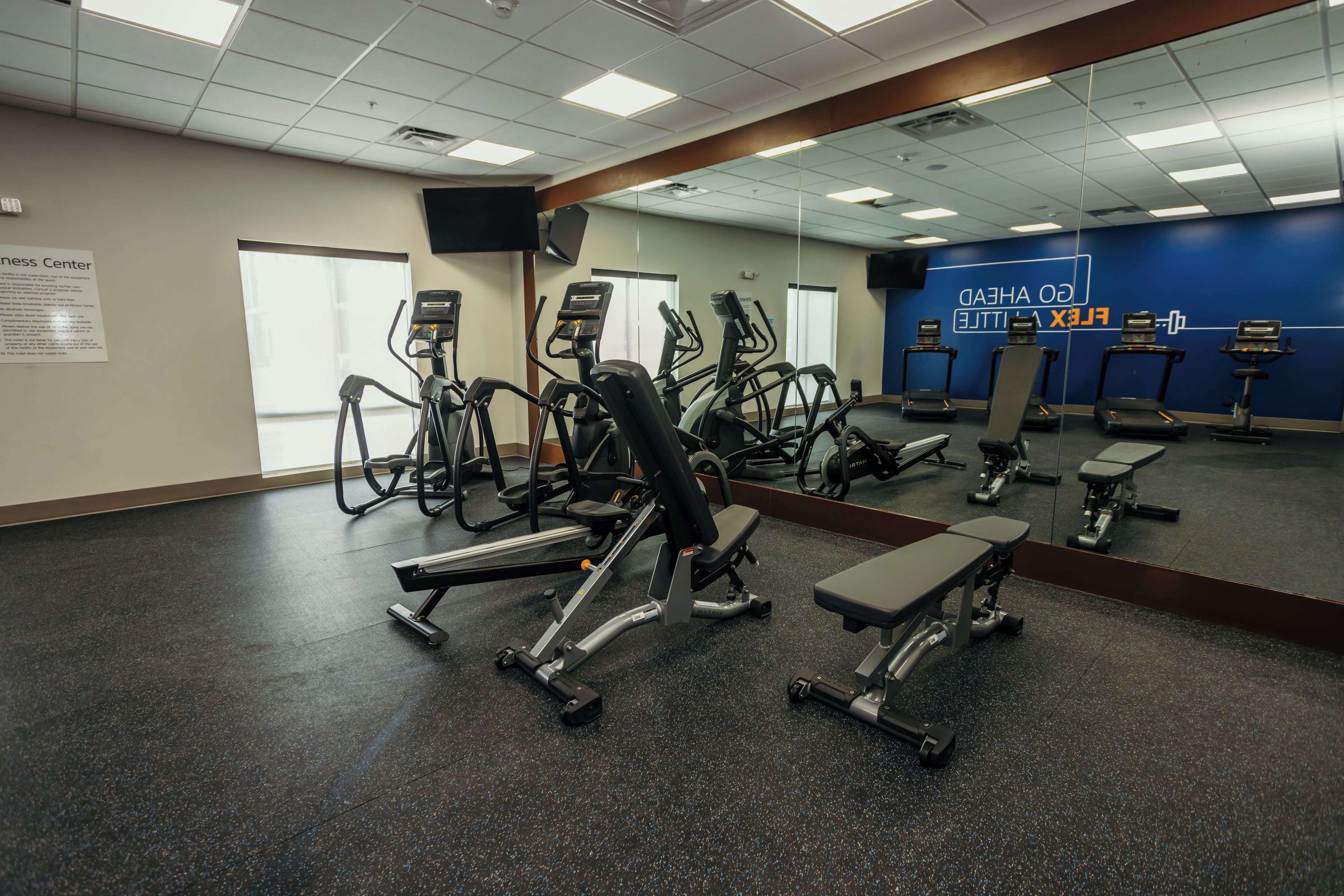 Un gimnasio con diversos equipos de ejercicio, incluyendo cintas de correr y máquinas de pesas, y un espejo grande en la pared.