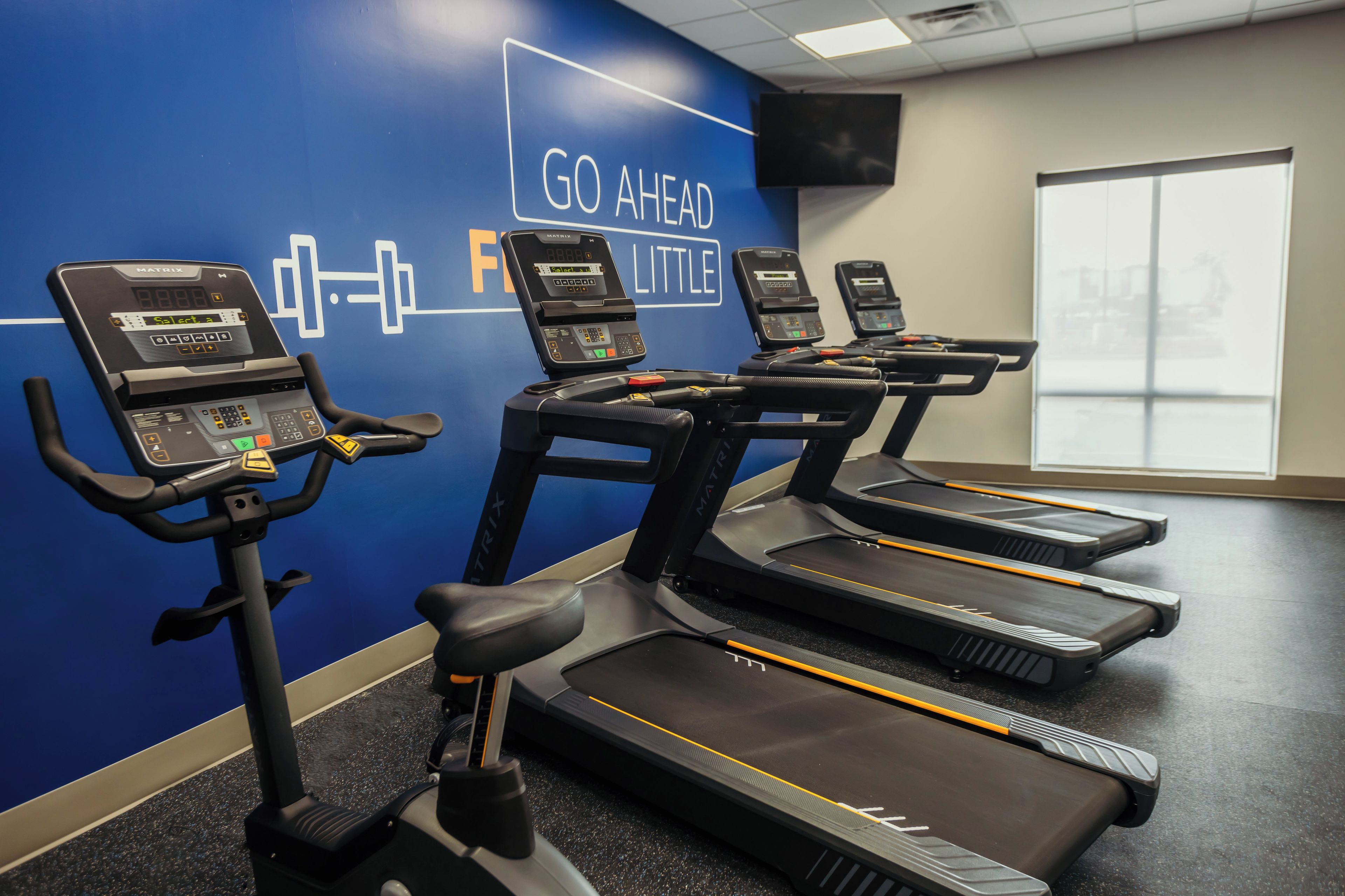 Une salle de sport équipée de tapis de course et d’un mur orné de messages motivants.