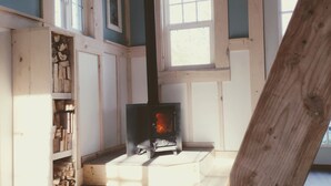 Um quarto com lareira a lenha, vigas de madeira no teto e janela com portaria branca.