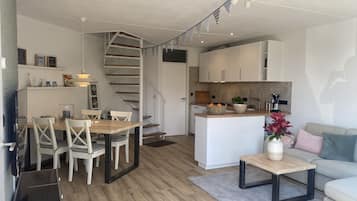 Compact living space with a central island kitchen and dining area, featuring a spiral staircase and self-catering amenities.