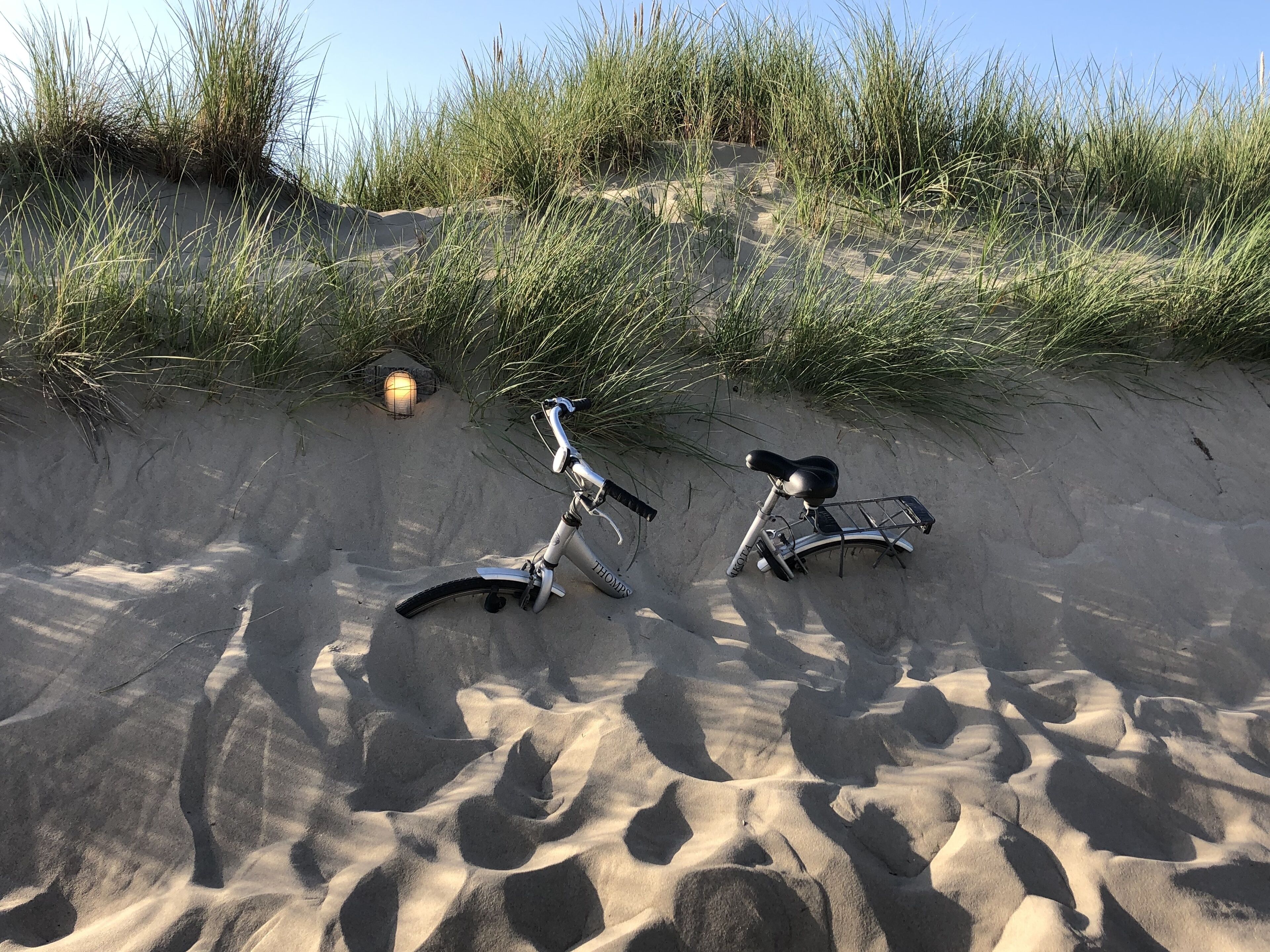A bicycle parked on a sandy beach with grass and a stone lantern in the background.