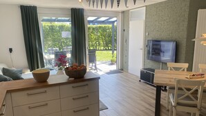 Ett modernt kök med en bänkskiva i trä, en matplats med ett träbord och stolar, en tv som är monterad på väggen och utsikt över trädgården genom en skjutdörr i glas.