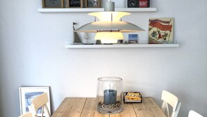 Ett matbord i trä med vita stolar, en vas i glas och en inramad tavla på väggen.