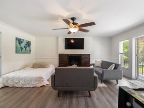 A modern living room with a fireplace, a ceiling fan, and a large window.