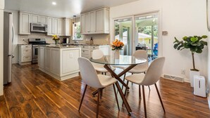 Une cuisine moderne avec des meubles blancs, un îlot central et un coin repas comprenant une table en verre et quatre chaises.