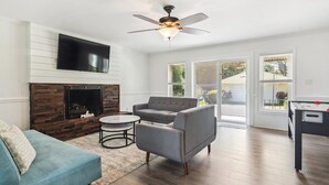 Un salon avec une cheminée, un canapé gris, une table basse ronde et un ventilateur de plafond.