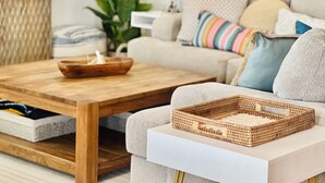 A modern living room with a sofa, a wooden coffee table, and a wicker tray. - Incredible Ocean Sunrise Views, Sleeps 12, Experienced VRBO Premier 5 STAR Host (Freeport)