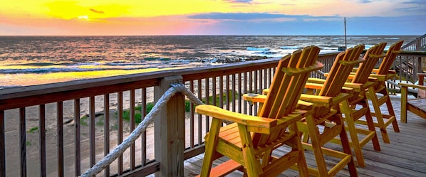 A wooden deck with a railing overlooking the ocean at sunset.