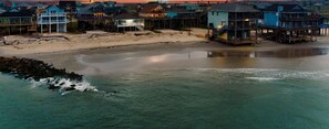 A coastal residential area with houses on stilts, a sandy beach, and a calm sea.
