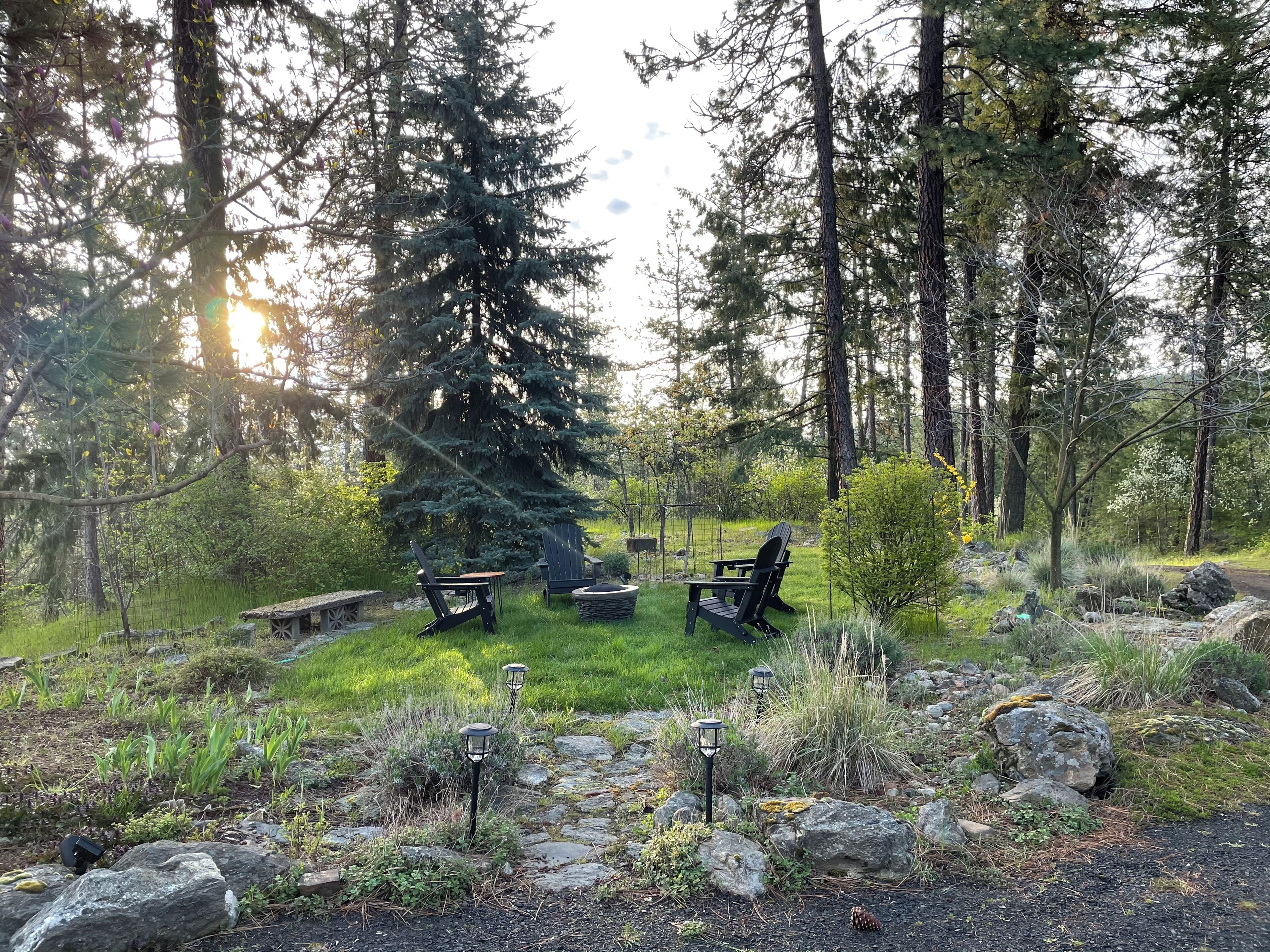 Un espacio al aire libre rodeado de follaje y rocas, con dos sillones Adirondack y un banco de piedra.