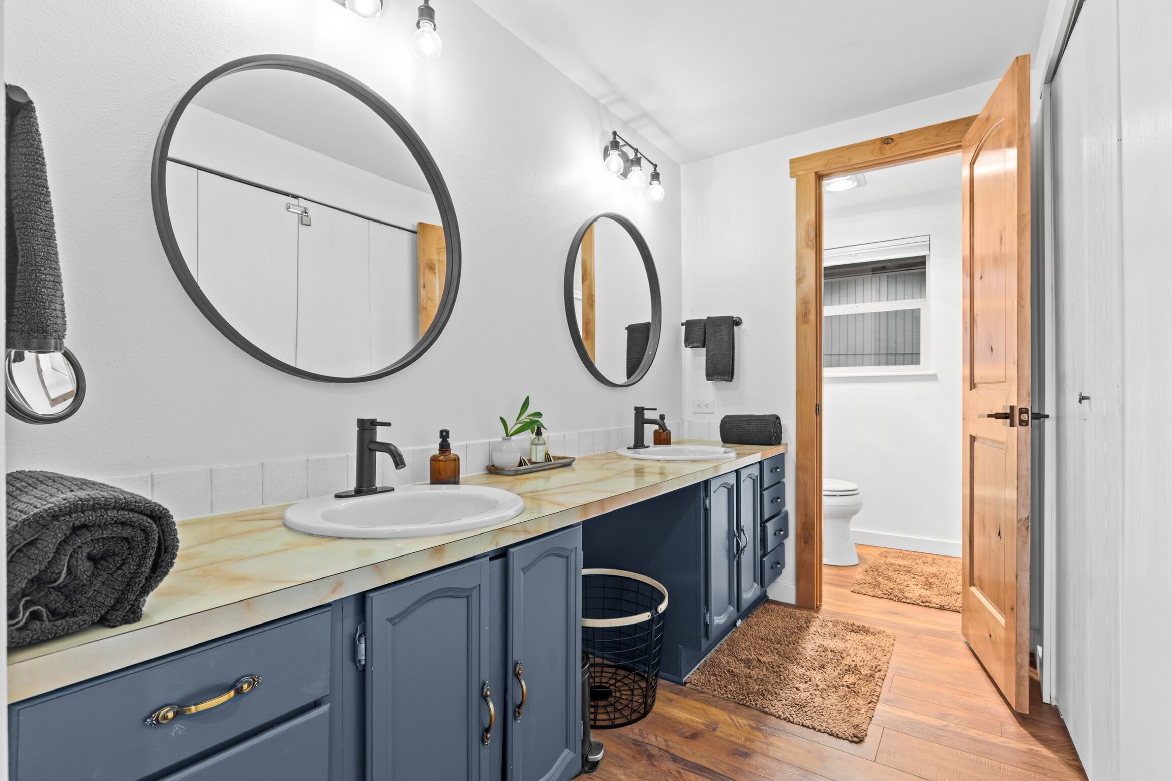 A modern bathroom with two sinks, a large mirror, and wooden flooring.