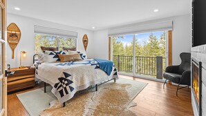 A modern bedroom with a large bed, a view of the outdoors, and a fireplace.