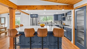 A modern kitchen with a central island, dark cabinetry, and a wooden ceiling.