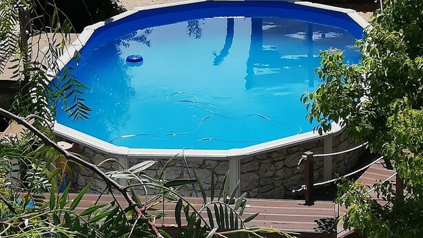 A swimming pool with a stone border and a wooden deck surrounding it. - Complesso di ville con piscina (porto cesareo)