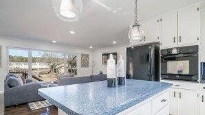 A modern kitchen with a blue granite countertop, white cabinetry, and stainless steel appliances. - Cheerful & Stylish 4 Bedroom Lake-Side House (Hot Springs)