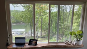 Een werkplek met een laptop en tablet op een houten plank, een stoel en een plant.