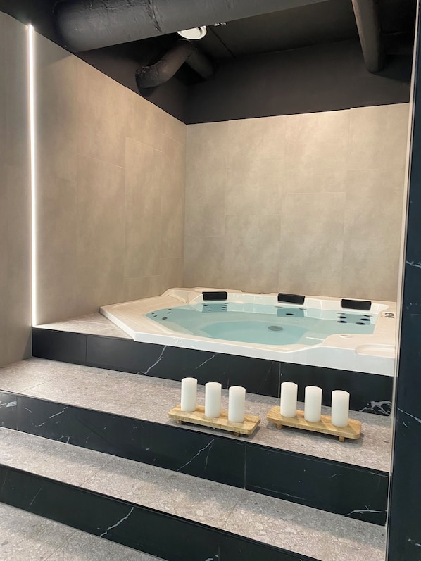 A modern bathroom with a large bathtub, a wooden bench, and a set of steps leading up to the tub.