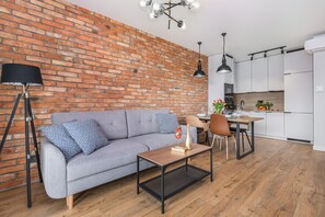 A modern living room with a brick wall, a grey sofa, a coffee table, and a dining area with a chair and table.