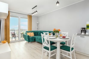 A modern living room with a green sofa, white chairs, and a dining table set for four.