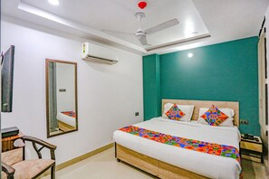 A bedroom with a bed, a ceiling fan, an air conditioning unit, a mirror, and a teal accent wall. - Fabexpress Rama (New Delhi)