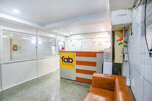 A hotel reception area with a sign for 'fab hotels,' a water dispenser, a brown leather couch, and a wall-mounted air conditioning unit. - Fabexpress Rama (New Delhi)