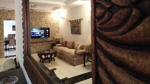 Uma sala de estar com parede de pedra, televisão fixada na parede, sofá e mesa de centro.