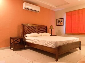 A bedroom with a wooden bed, a nightstand, a lamp, an air conditioner, and a window with curtains. - Morgah Resort Villas (Rawalpindi)