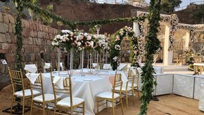 Decoração de casamento ao ar livre com mesas redondas, cadeiras douradas e flores.