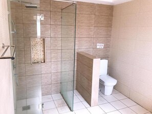 A bathroom with a glass shower enclosure, a toilet, and a tiled floor. - Morgah Resort Villas (Rawalpindi)