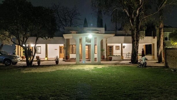 Um edifício moderno com uma estrutura iluminada no centro, rodeado por um gramado bem cuidado e árvores.
